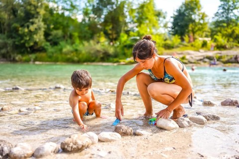 Mother and son enjoying family holidays, playing with toy cars by the river on a sunny summer day