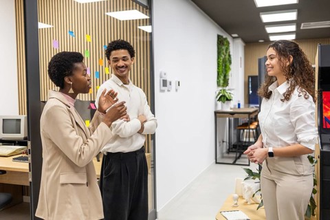 Three colleagues engage in a lively discussion in a stylish office environment with colorful sticky