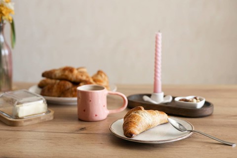 A freshly baked homemade croissant sits invitingly on a plate, accompanied by a pink mug and a