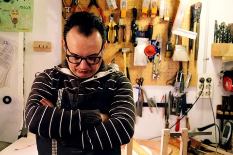A luthier stands thoughtfully in his workshop, surrounded by tools and materials for crafting bass