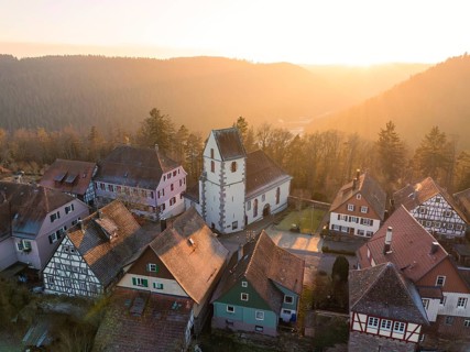 A village with half-timbered houses and church in soft light embedded in a natural landscape,