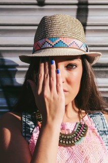 A woman wearing a straw hat with a vibrant geometric band shields one eye with her hand. She sports