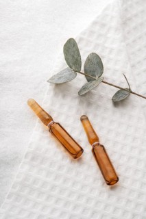Elegant glass ampoules filled with anti-aging serum for face care, displayed on a textured white