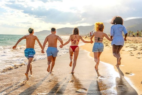 Five multi ethnic friends running on the beach at sunset holding hands, enjoying summer vacation