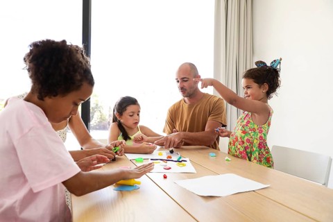 A family engages in creative activities at home, working with colorful modeling clay at a wooden