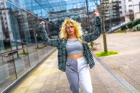 Young woman with curly hair dancing energetically in a modern city environment, showcasing vibrant