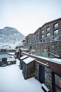 A serene winter scene showing a stone building nestled against a snow capped mountain in Andorra.