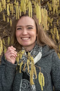 Happy young Caucasian woman without allergy problem standing by flowering hazel bush in Ystad,