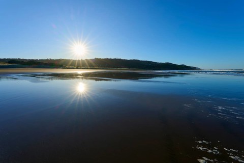 Early morning sun rays reflecting on the calm sea surface on a clear beach, Muriwai Beach,