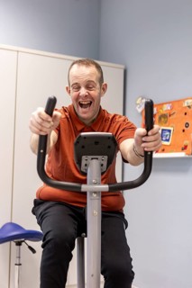 A joyful individual using an exercise bike at a day center designed for people with disabilities.