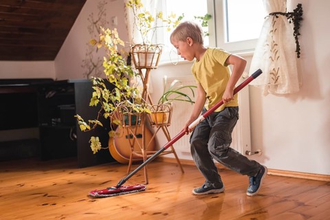 A 6-year-old boy cleaning the wooden floor with a mop