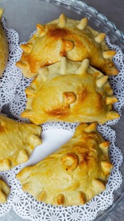 Close-up of golden brown, homemade baked empanadas with decorative edges and stamped tops, arranged