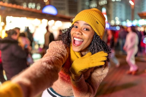 Young woman wearing yellow winter clothes taking selfie at christmas market, enjoying festive
