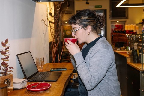 A woman enjoys a cup of specialty coffee while working on her laptop in a cozy, modern cafe. The