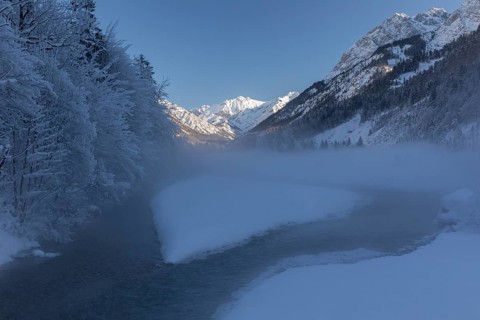 The Riss creek flowing through a snow covered landscape in the Eng valley. Sunny day with blue sky.