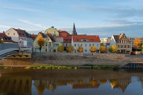 Colourful buildings by the river with autumn trees reflecting in the water in the evening light, a