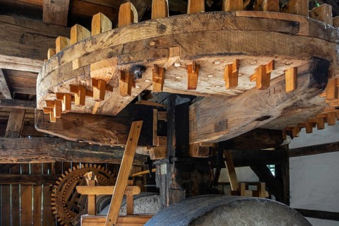Wooden cogwheels and gear mechanism inside 18th century watermill, water wheel at open air museum