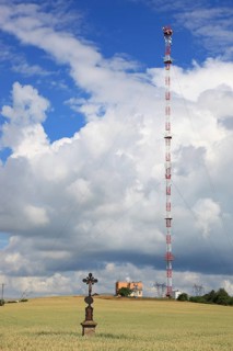 Wheat field, grain field with a lonely field cross, in the background transmitting station with