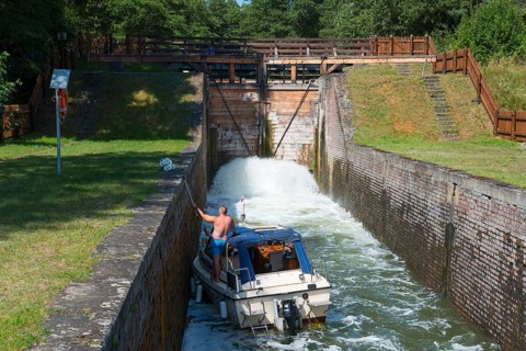 A boat passes through a water-filled lock surrounded by brick walls and lush greenery, Sluza
