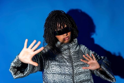 Fashionable woman wearing futuristic sunglasses and patterned jacket making stop gesture with hands