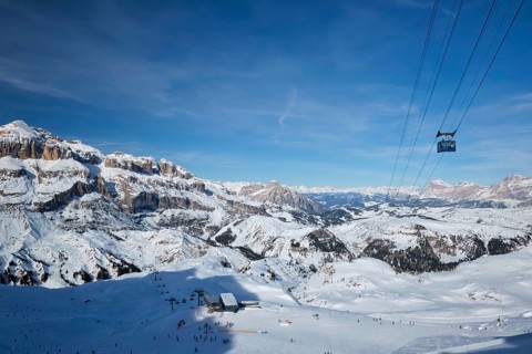 View of a ski resort piste with people skiing in Dolomites in Italy with cable car ski lift. Ski
