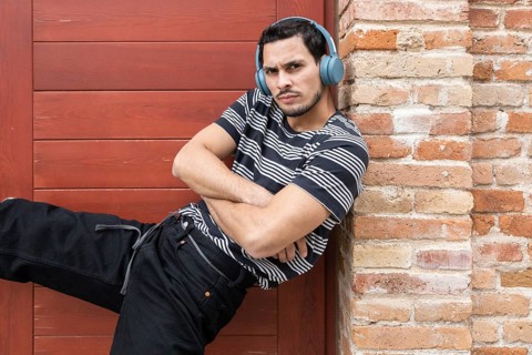 Young Cuban man in a striped shirt and headphones striking a dance pose against a brick wall.
