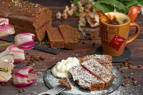 Cake with crumble and icing sugar next to whipped cream and cup with sparkling coffee, flower