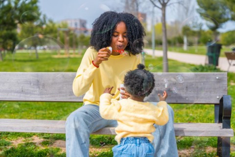 Frontal three quarter length photo of an african woman and daughter playing with soap bubbles in a