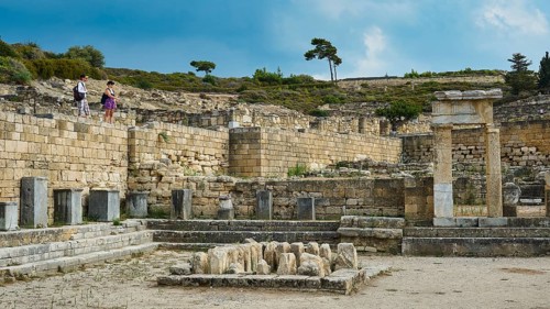 Historic ruins with several stone structures and few visitors under blue sky, ancient well house,