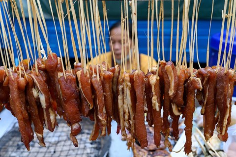 Strips of meat hang to dry in the sun ready to be grilled at a Bangkok Chinatown street food stall,