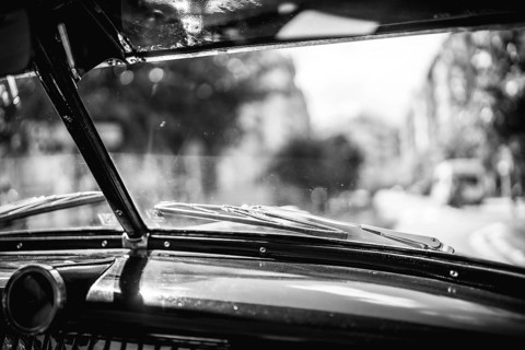 A black and white photo of a car window with a city in the background. Scene is nostalgic and