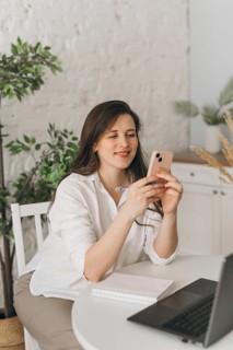A nutritionist sits at a table with a laptop, phone, and notebook, engaging in a virtual