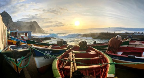 Fishing boats on the shore with dramatic sunset in the background, waves making waves across the