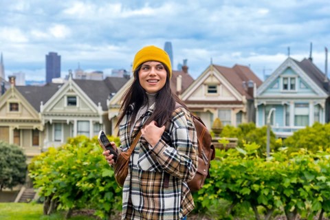 Woman traveler exploring alamo square while carrying a backpack and holding a smartphone, enjoying