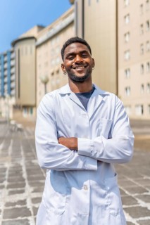 Vertical portrait of a smiling african doctor standing with arms crossed outside the hospital