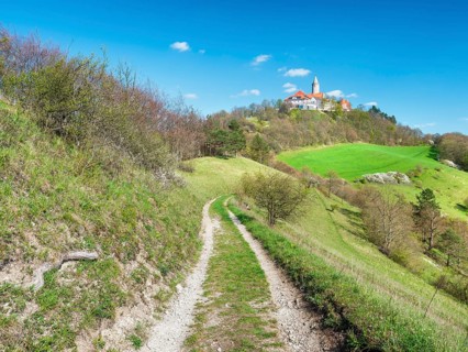 View of hilly landscape with green meadows and forests in spring, hiking trail leads to