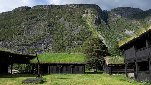 Traditional wooden houses with grass sod roofs in front of a cloudy mountain landscape, backdrop