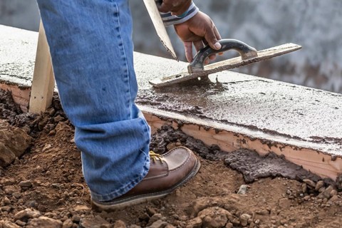 Construction Worker Using Wood Trowel On Wet Cement Forming Coping Around New Pool