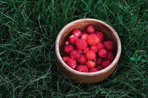 A wooden bowl filled with ripe red strawberries placed on lush green grass, capturing the essence