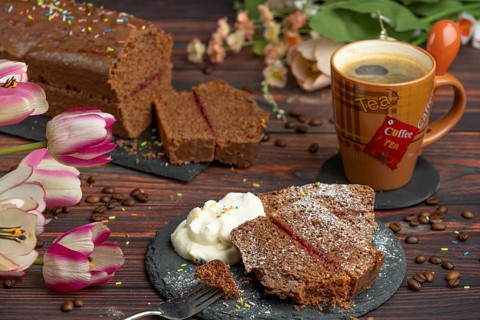 A slice of chocolate cake next to a cup of coffee decorated with tulips and whipped cream