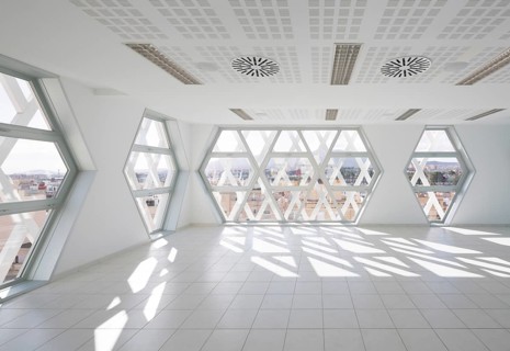Modern auditorium interior featuring geometric, hexagonal windows. Bright natural light floods the