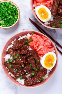 Gyudon Japanese beef with rice, pickled ginger, boiled egg slice, garnished with green onions, in a