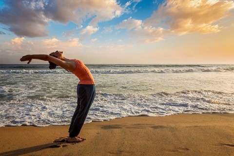 Young woman doing yoga Sun salutation Surya Namaskar pose Hasta Uttanasana on tropical beach on