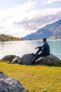 Man sitting on rocks on the lakeshore and enjoying the peaceful mountain landscape, Lake Brienz,