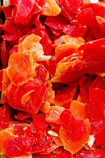 Close up of thinly sliced and vibrant dried papayas. The vivid red and orange hues create a