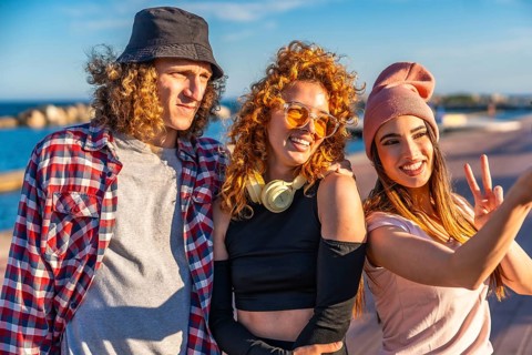 Three fashionable young friends taking a cheerful selfie while enjoying a sunny day by the seaside,