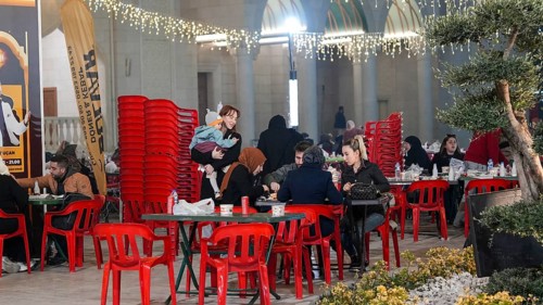 Muslim families and individuals gather at outdoor tables for a mass community Iftar meal under