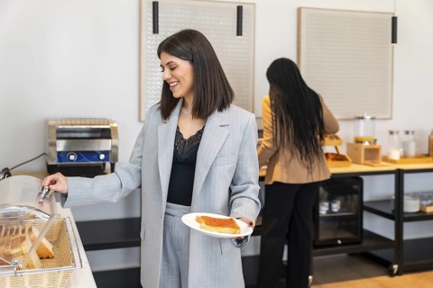 Businesswoman smiling while choosing food from breakfast buffet in hotel during business trip,