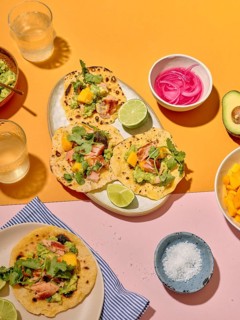Top view of colorful taco preparation on a vibrant yellow and pink background, featuring fresh