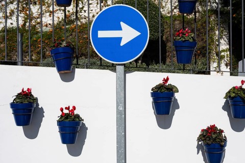 Traditional white Andalusian wall with blue flower pots, red geraniums, and a blue turn right road